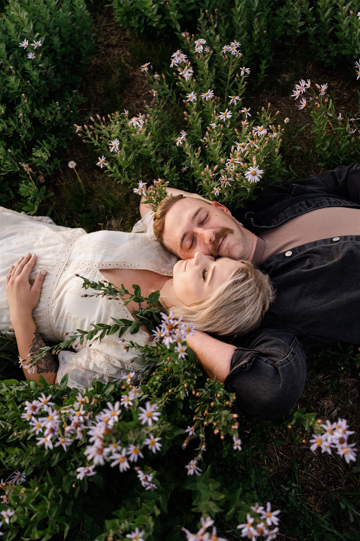 Engaged couple laying in wildflowers smiling at each other