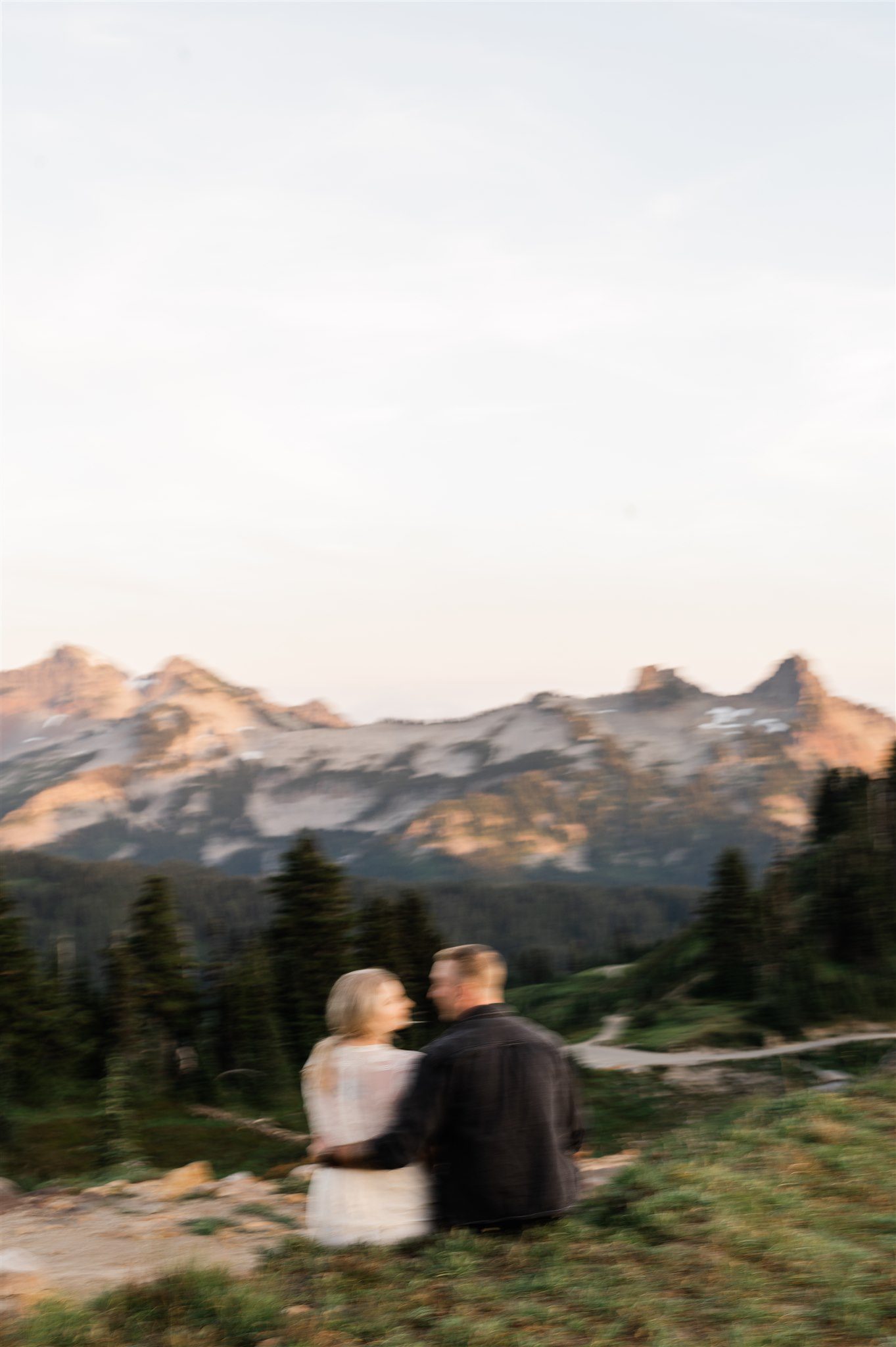 Blurred photo of couple sitting with mountains and trees in the background at sunset