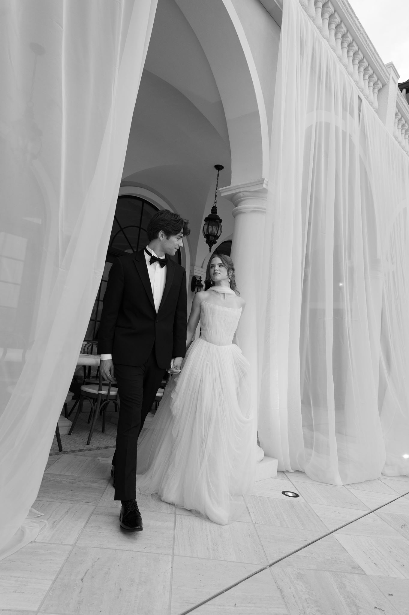 Bride and groom emerging from flowy draping on a terrace